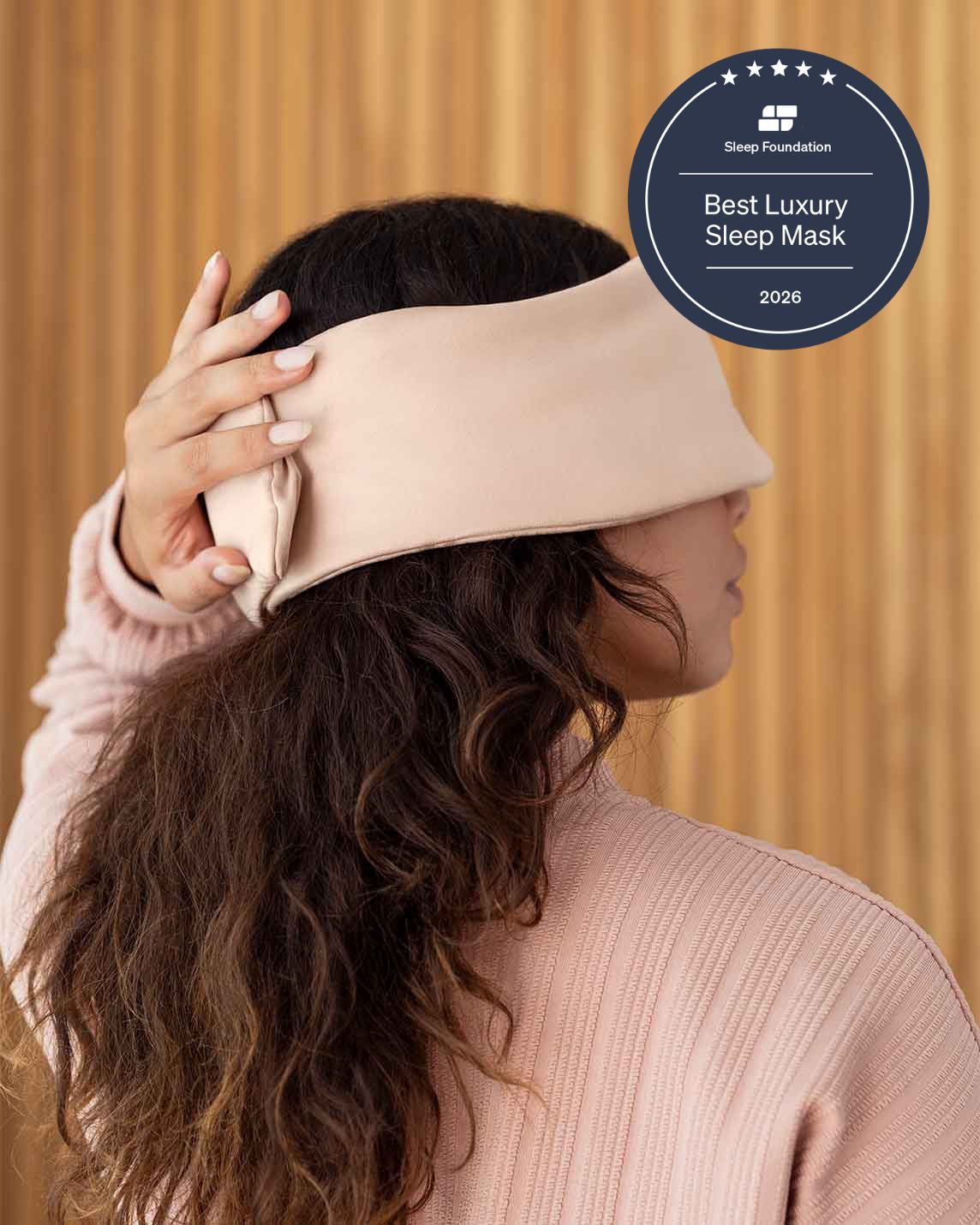 A photo from the side of a woman with long brown hair holding her hand over the back of a silk sleep mask. [44377020825819, 46730820944091, 46730821009627, 46730821075163, 46730821140699, 47185819467995]