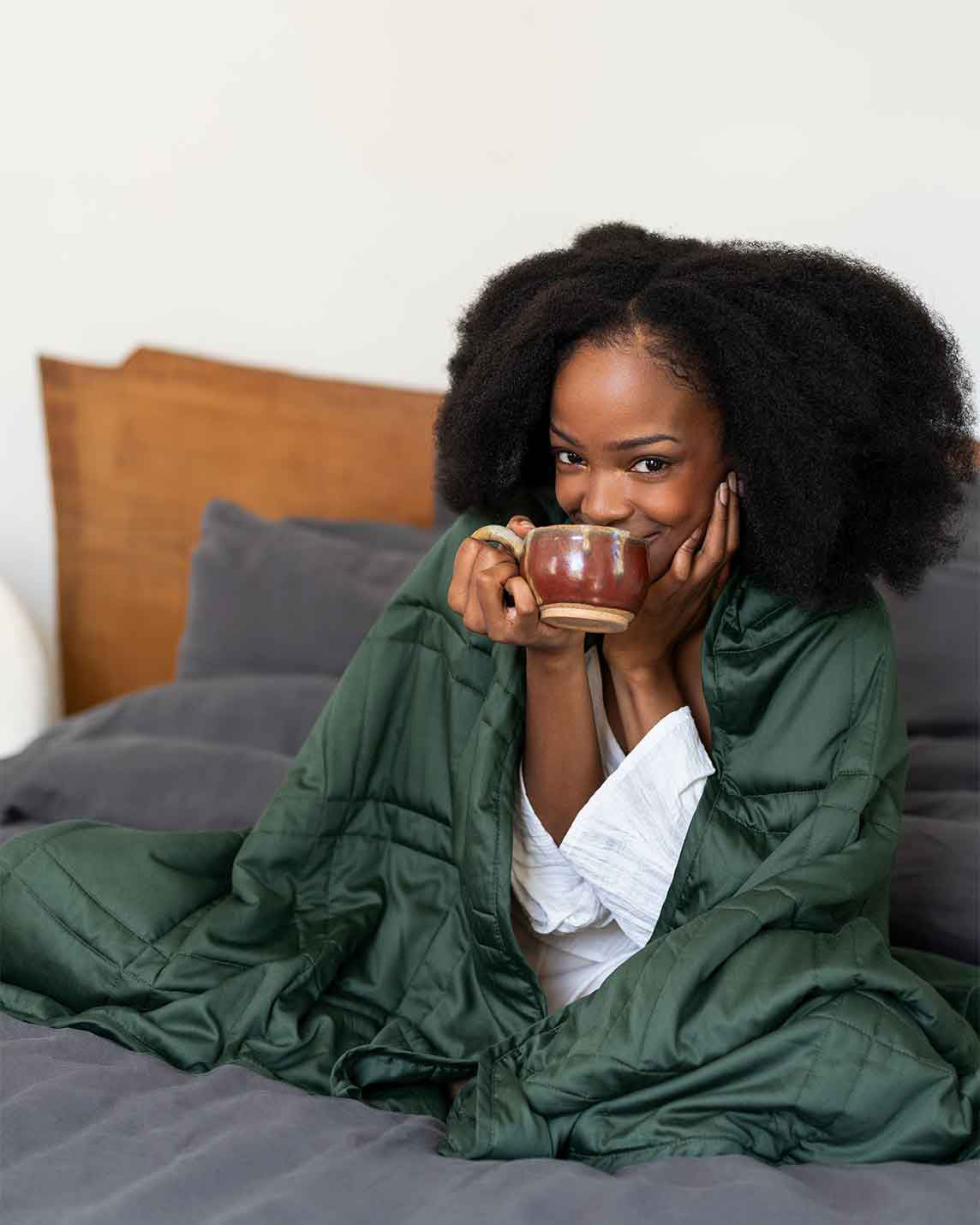 A woman smiles and takes a sip of coffee with a spruce green weighted blanket wrapped around her shoulders [46061921730779, 46061921763547, 46061921796315, 46063267709147, 46063269118171, 46684279668955, 47185820188891, 44422820561115, 47185820156123, 44422818234587]