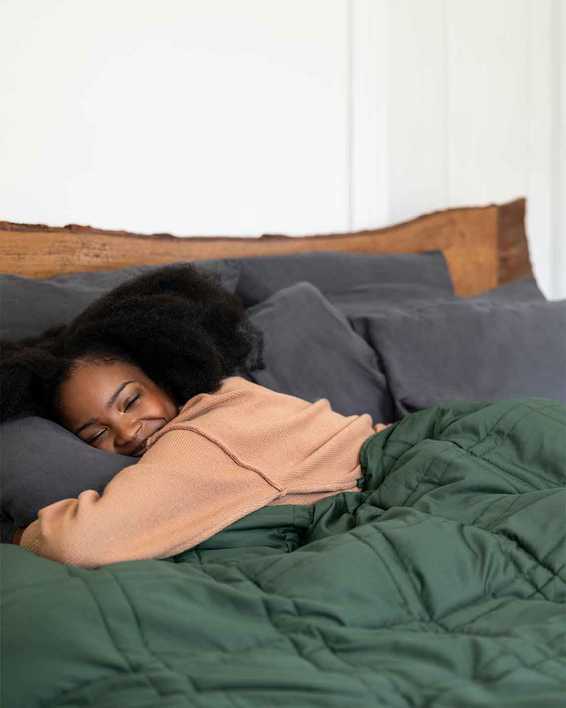 A woman smiles with eyes closed, hugging a pillow under a spruce green weighted blanket [44422820561115, 45574418333915, 44422814826715, 46452818542811, 44422813090011, 46452818575579, 44422818234587, 46452819099867, 46684279668955, 47185820188891, 47185820090587, 47185820057819, 47185820156123]