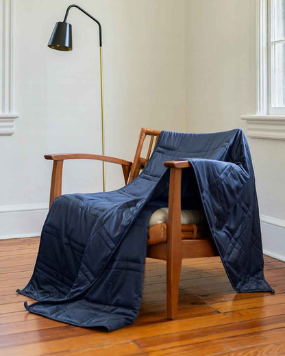 A blue weighted blanket across a chair next to a lamp. [43649942782171, 45574417875163, 44422804340955, 45574418137307, 44422811287771, 46452818510043, 44422816432347, 46452819067099, 47185820123355, 47185819992283, 47185820025051, 47185819762907, 46301293543643, 46301293773019, 46301293805787, 46301293904091]