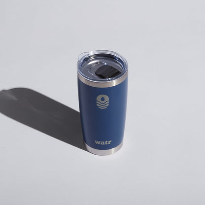 Blue 20 oz WATR tumbler with logo, featuring a clear lid, displayed on a light surface with a shadow to the side.