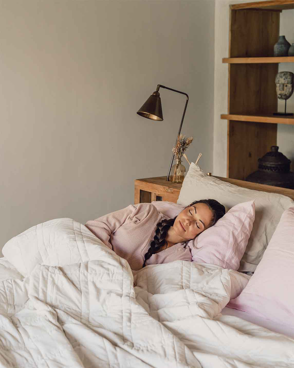 A young woman with a braid sleeps peacefully in a bed with a pink pillowcase and a white weighted blanket across her body.  [42934587818203, 45574417940699,42934587850971, 46452818444507, 42934587883739, 46452819001563, 47185819795675, 47185819861211, 47185819926747]