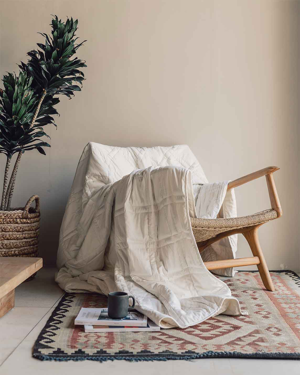 A luxurious looking white cotton weighted blanket drapes across a chair, next to a coffee mug on the floor and a plant. [42934587818203, 45574417940699, 42934587850971, 46452818444507, 47185819795675, 47185819861211]