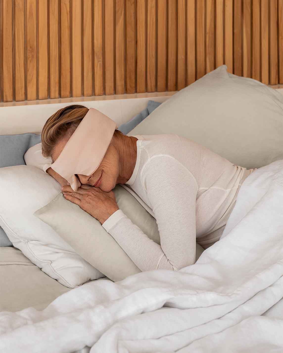 A senior woman with blonde hair rests her head on a pillow wearing a silk sleep mask [44377020825819, 47185819467995]