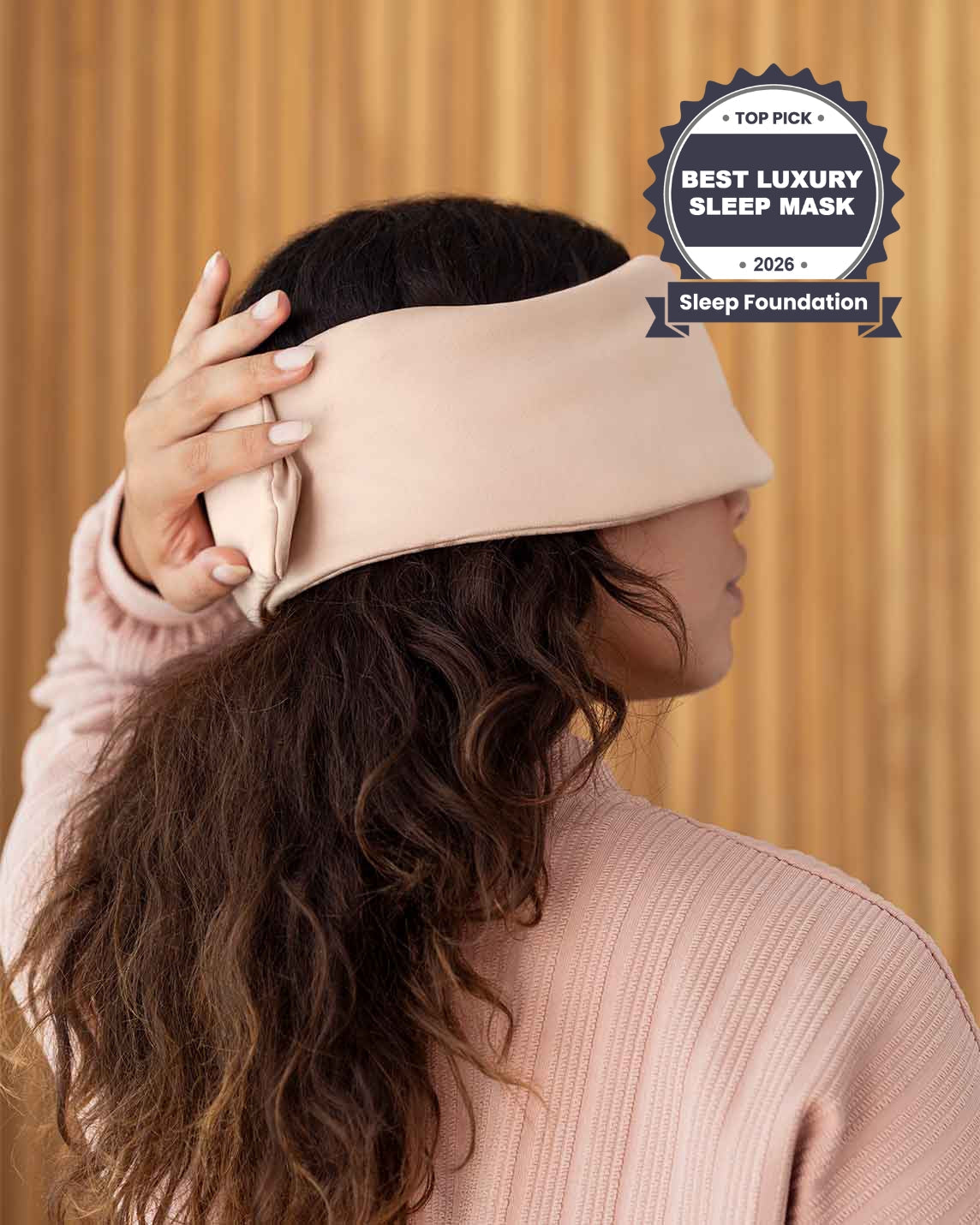 A photo from the side of a woman with long brown hair holding her hand over the back of a silk sleep mask. [44377020825819, 46730820944091, 46730821009627, 46730821075163, 46730821140699, 47185819467995]