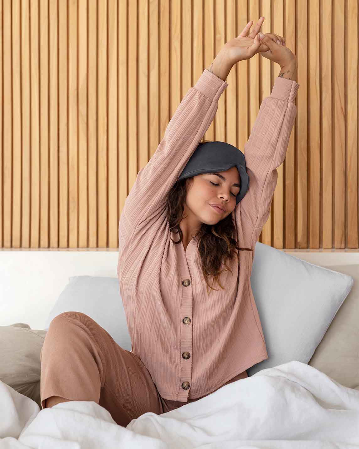 A young woman reaches up stretching wearing a silk sleep mask on her head [44377020793051, 47185819435227]