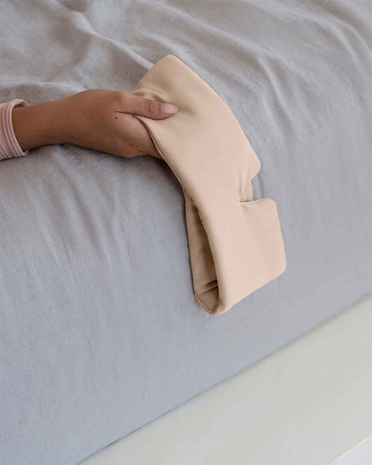 A young woman holds a silk sleep mask in pink off the side of the bed [44377020825819, 46730820944091, 46730821009627, 46730821075163, 46730821140699, 47185819467995]