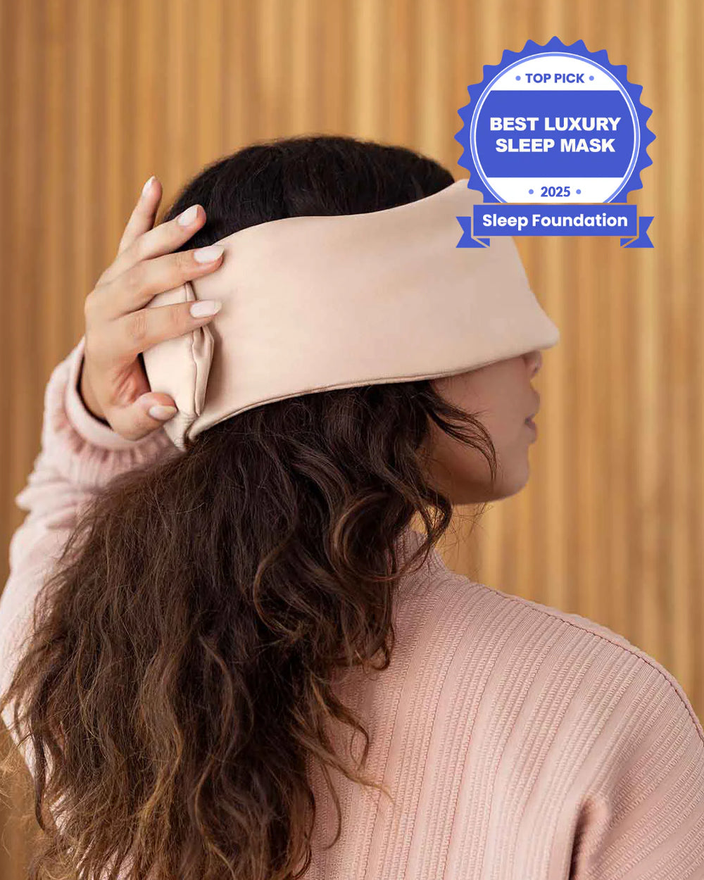 A photo from the side of a woman with long brown hair holding her hand over the back of a silk sleep mask. [44377020825819, 46730820944091, 46730821009627, 46730821075163, 46730821140699, 47185819467995]