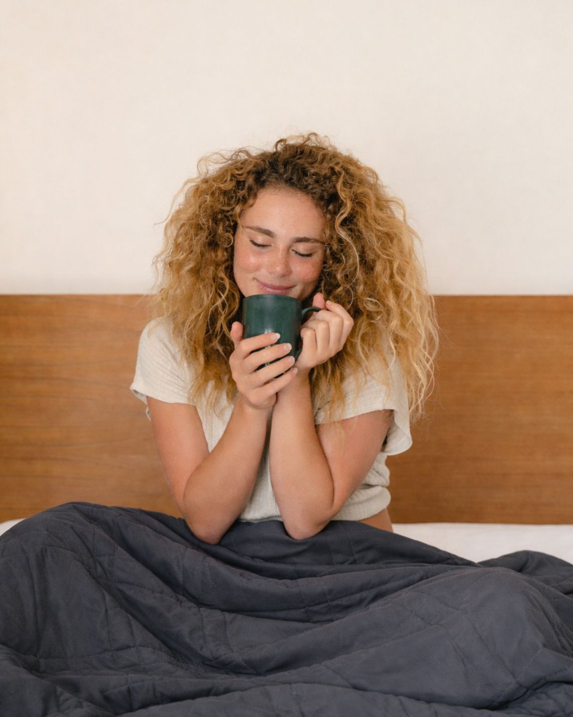 Woman sitting on a bed holding a mug, wrapped in a midnight blanket [48904789885147]