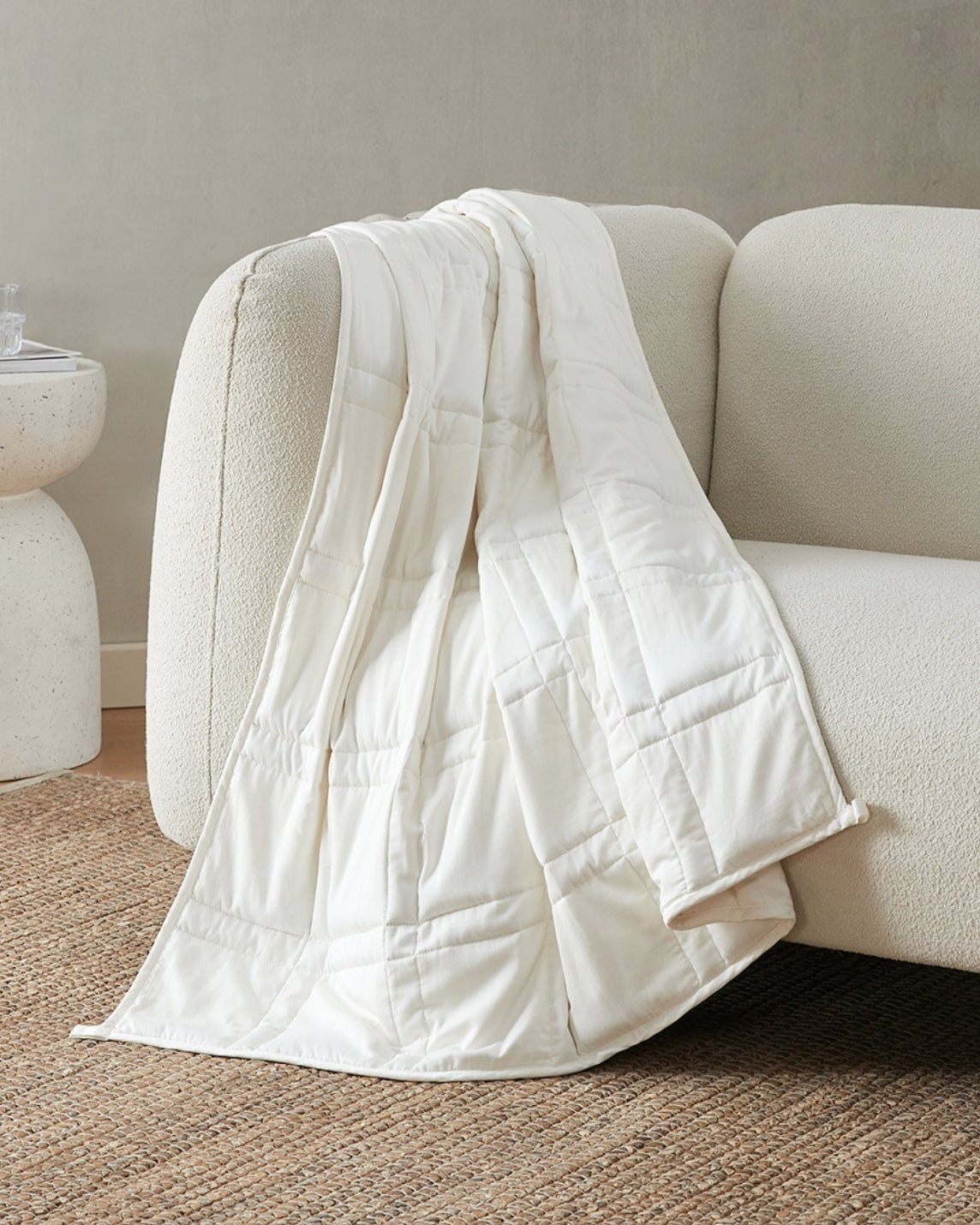 pebble white weighted blanket draped over the arm of an ivory sofa [42934587621595]